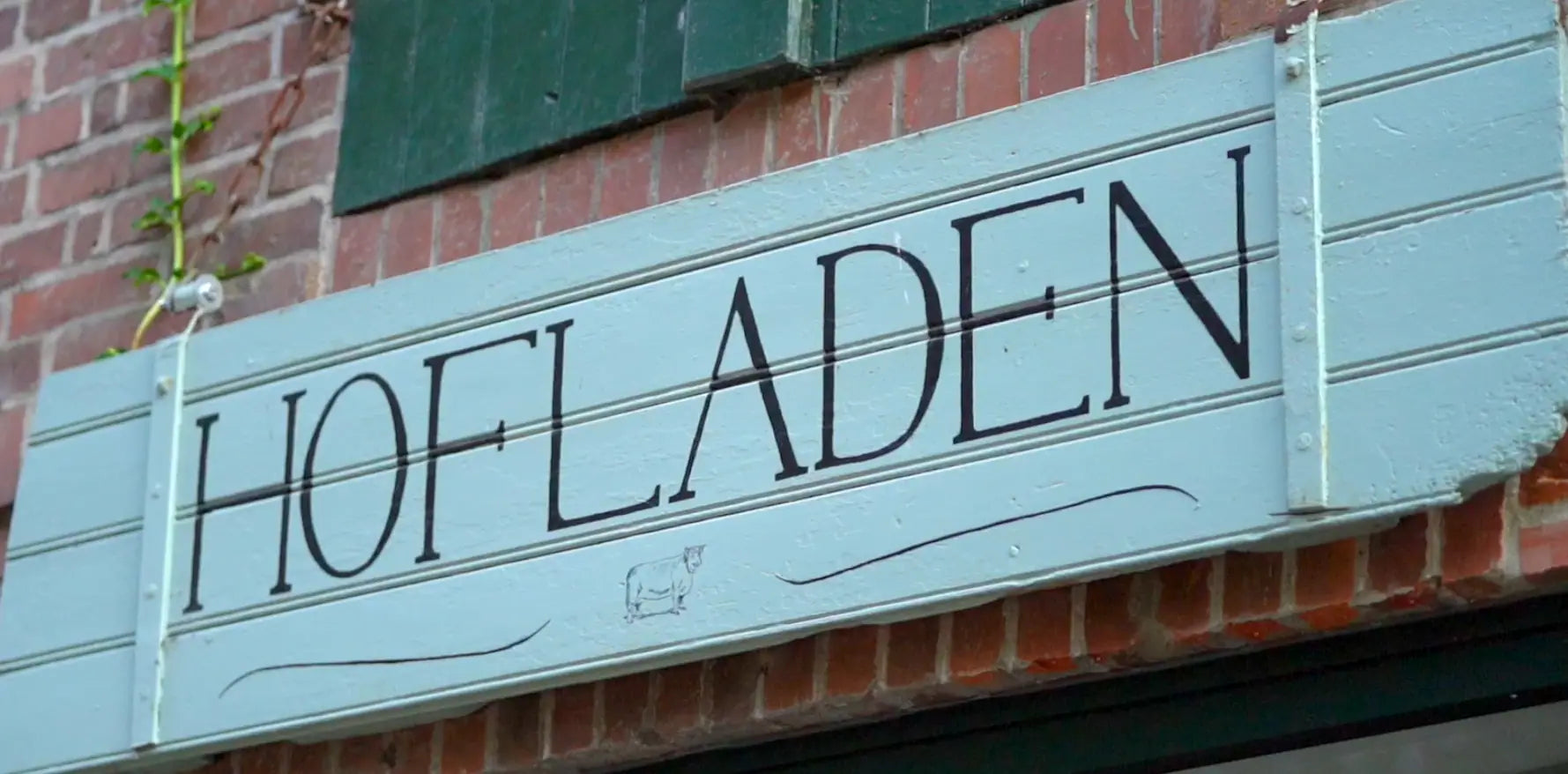 Türkisfarbenes Holzschild mit der Aufschrift Hofladen vom Hofladen Tante Klüver auf dem Lindenhof in Travenhorst